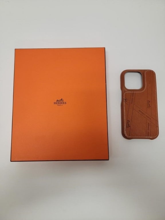 HERMES EMBOSSED BROWN LEATHER IPHONE 15 PRO CASE: Hermes embossed brown leather iPhone 15 pro case. Measures 6" x 3" x .5". Includes original orange box. Condition is good with no signs of use, see images. Weight: 8 oz.