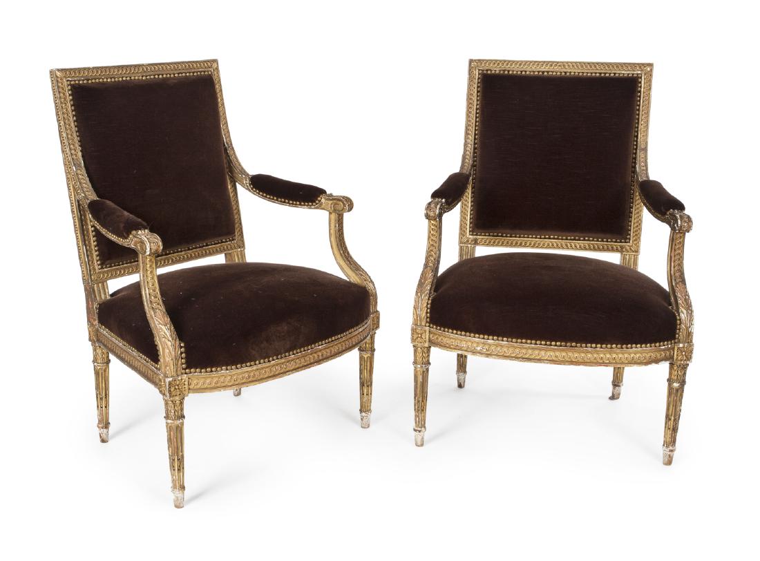 PAIR OF LOUIS XVI STYLE GILTWOOD ARMCHAIRS: A pair of heavily carved and gilt armchairs with cordovan velvet upholstery and nailhead trim. Each, 37 by 27 by 19 inches Categories: Tommy Hilfiger