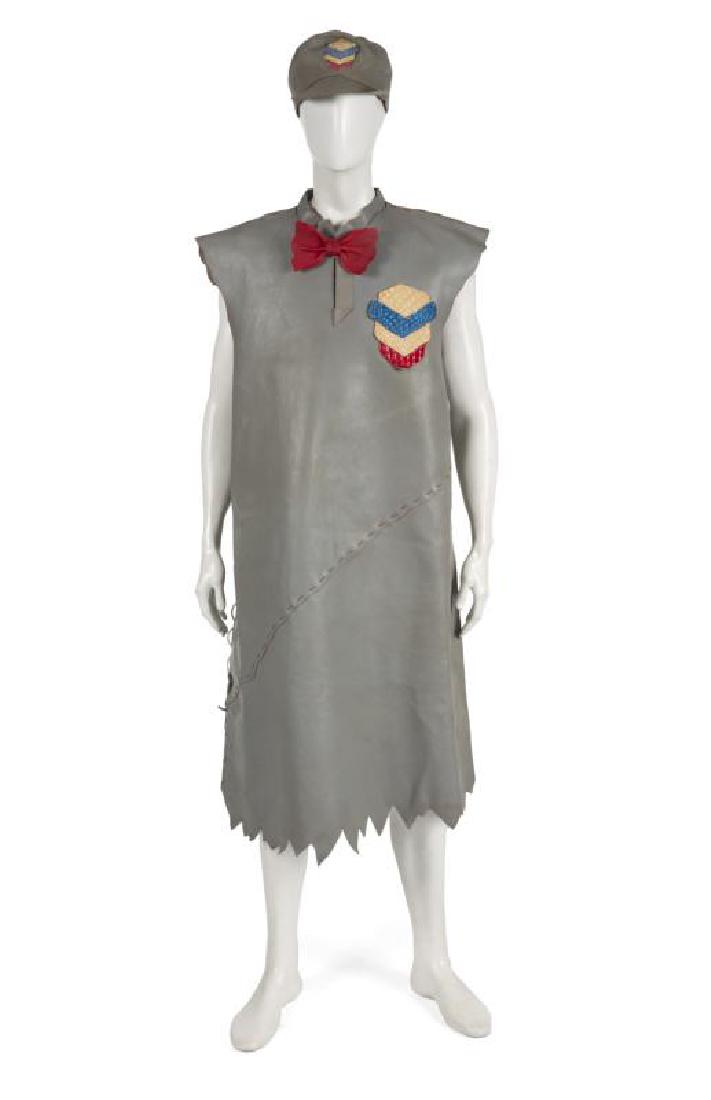 RICK MORANIS THE FLINTSTONES COSTUME: A blue grey Chevrox leather tunic and cap worn by Rick Moranis as Barney Rubble in The Flintstones(Universal, 1994). The tunic has mock crocodile Chevrox logo and a red leather bow tie. Costume design