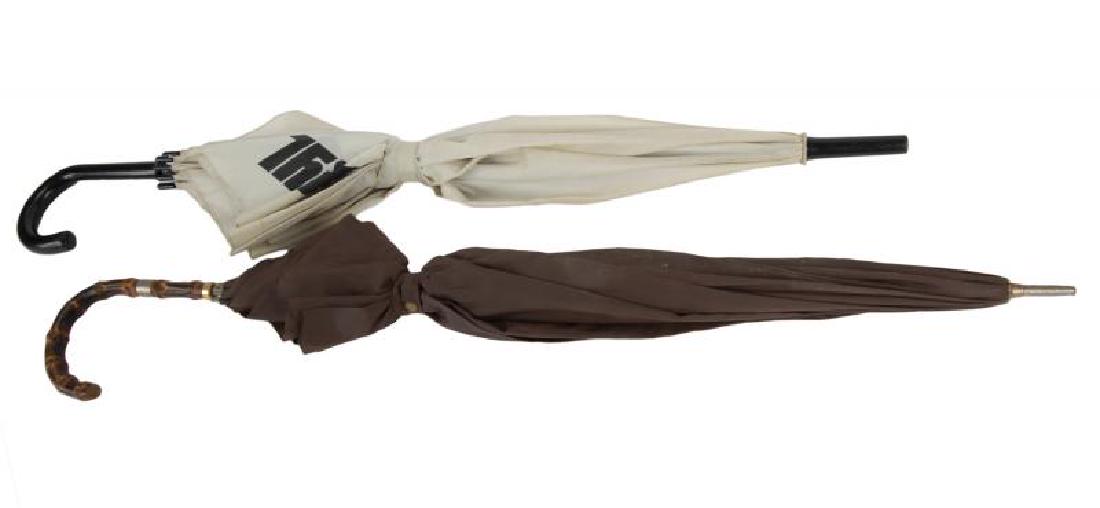 GRETA GARBO UMBRELLAS: A pair of umbrellas: one in light grey with "THIRTEEN" stamped in black, with black handle; one in brown with a carved wood handle. Longer, 34 1/2 inches PROVENANCE From the Estate of Greta Garbo <