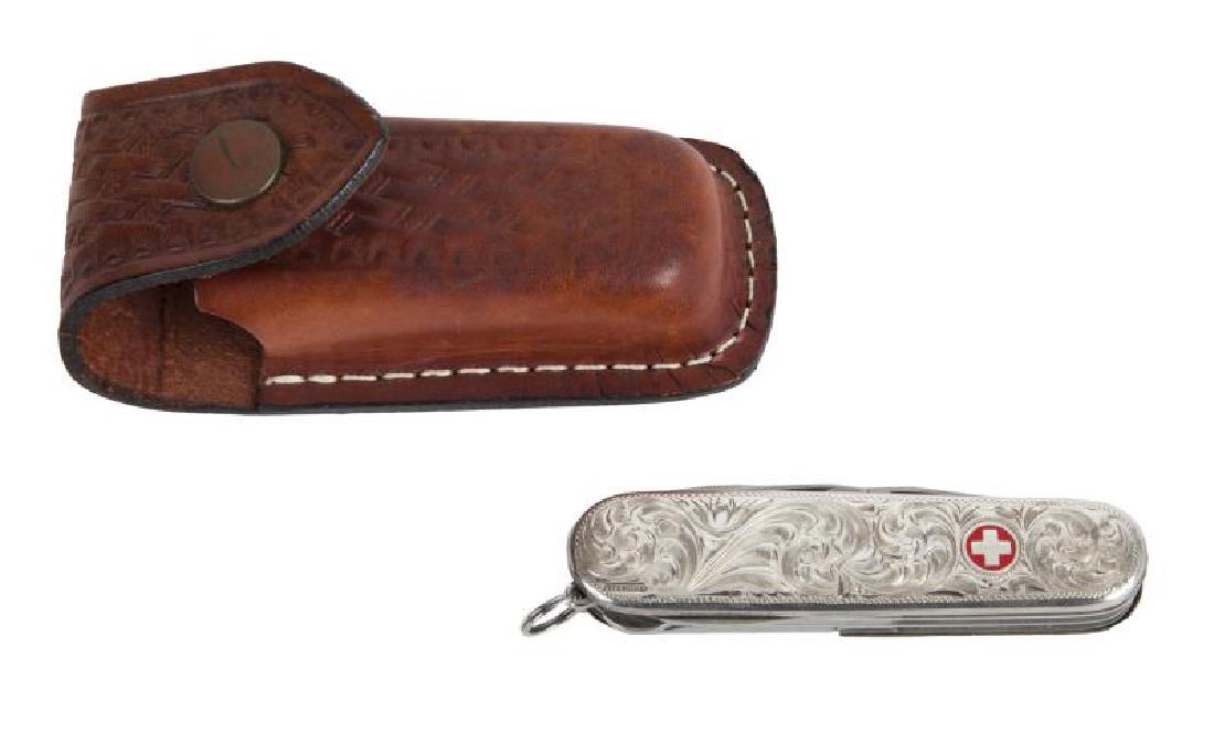 BURT REYNOLDS FANCY SWISS ARMY KNIFE: A sterling silver piece with beautiful Western-style engravings, blade marked in part "Victorinox / Switzerland / Officier / Suisse;" housed in its own brown leather case.; PROVENANCE From the Estate 