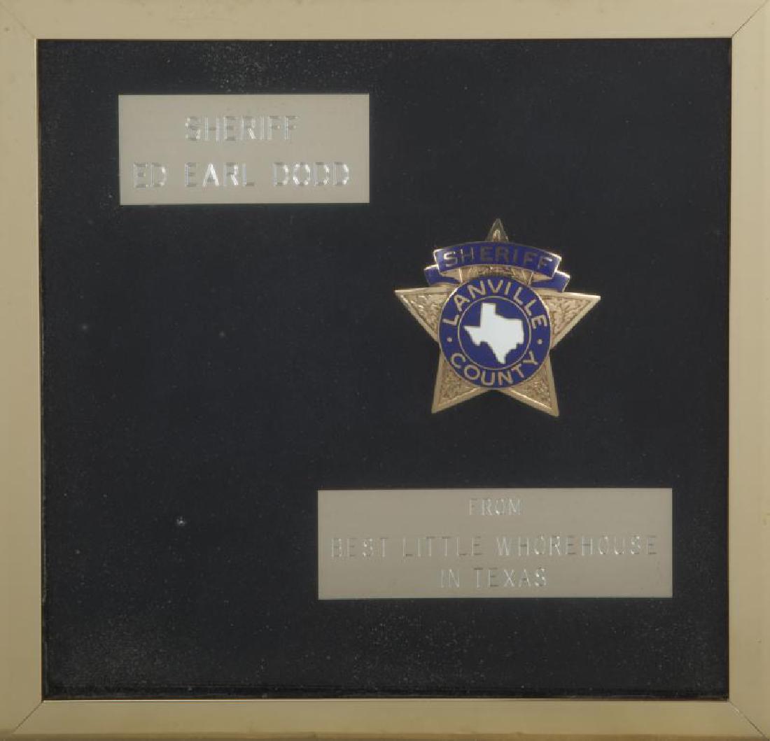 BURT REYNOLDS BEST LITTLE WHOREHOUSE IN TEXAS SHERIFF: A brass and enamel piece with text reading “Sheriff / Lanville County” mounted within a shadow box together with two plaques noting in part Reynolds' character name of "Sheriff Ed Earl Dodd;" one 