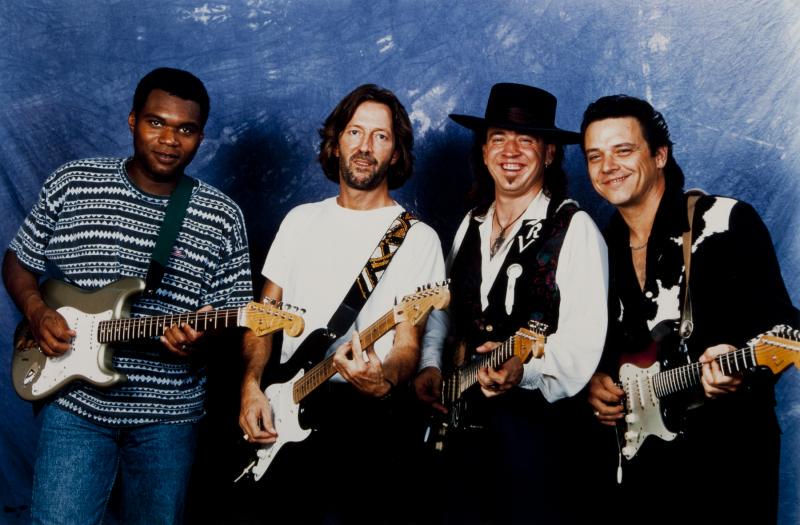 STEVIE RAY VAUGHAN ERIC CLAPTON PROMOTIONAL PHOTOGRAPH: A poster-sized color photograph taken by Robert M. Knight featuring Eric Clapton and Stevie Ray Vaughan with Robert Cray and Stevie's brother, Jimmie Vaughan. The image is especially poignant consider