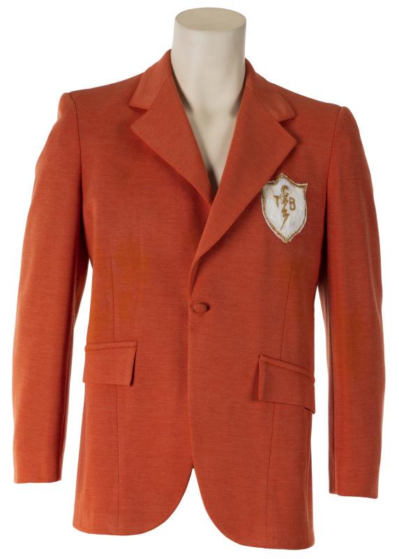 ELVIS PRESLEY TOUR JACKET • °: An orange jacket with "TCB" logo patch on the left chest, used in the late 1960s by Elvis' entourage. A JC Costume Co. label is present. Size 40. Accompanied by a letter of authenticity from Jimmy Vel