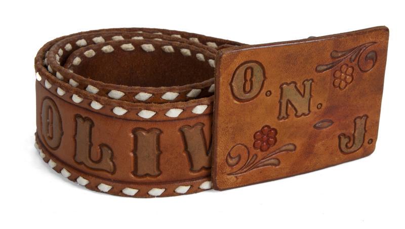 OLIVIA NEWTON-JOHN PERSONALIZED LEATHER BELT AND SIGNED: A 1970s embossed leather belt with floral motif that reads "Olivia" and a buckle that is embossed "O.N.J." The interior is engraved "Tom Pepera." Accompanied by an image of Olivia Newton-John wearing 