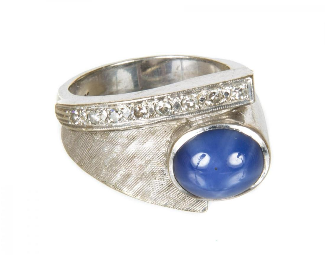 JAMES BROWN GOLD AND SAPPHIRE RING: A 14K white gold ring with a single lattice diffusion treated blue star sapphire weighing approximately 2.5 ct. next to a line of eight round diamonds totaling approximately 0.18 ct. Size 7 1/2, 9.2 g