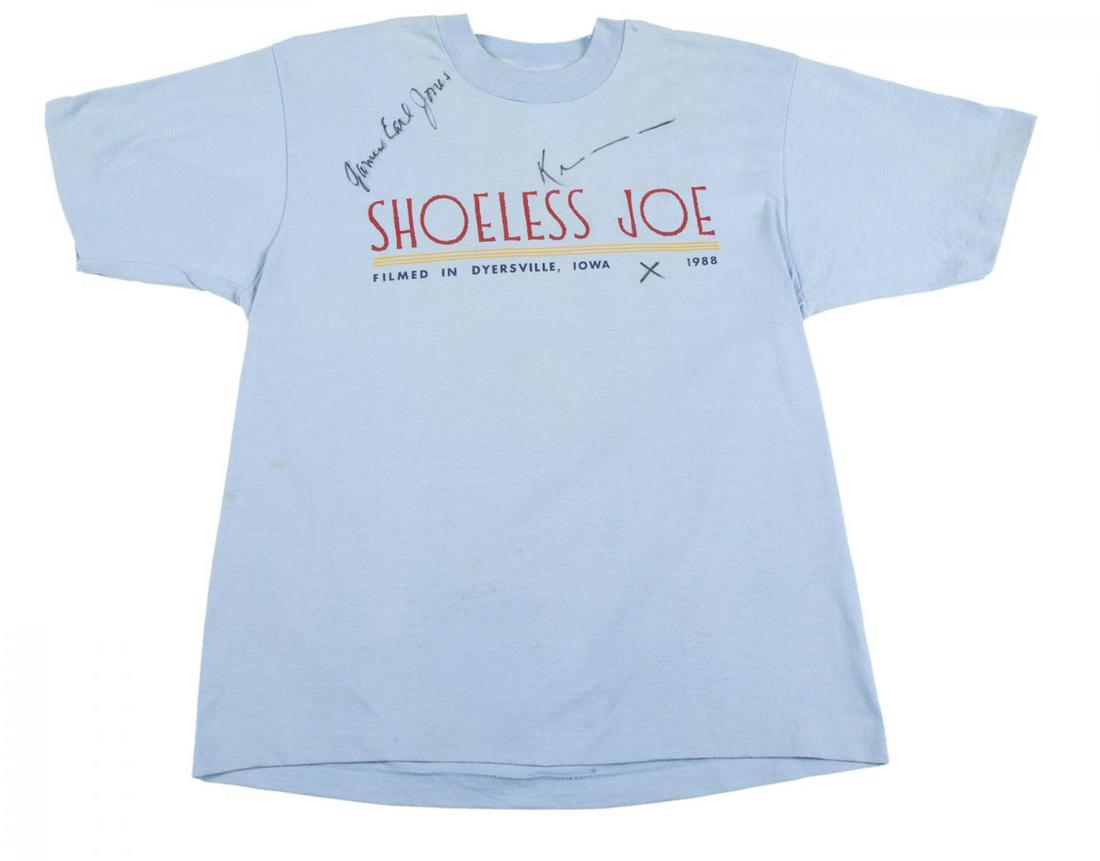 KEVIN COSTNER AND JAMES EARL JONES SIGNED T-SHIRT: A light blue cotton-polyester blend T-shirt, with text on the front reading “Shoeless Joe/ Filmed in Dyersville, Iowa 1988,” signed above in black felt-tip ink “James Earl Jones̶