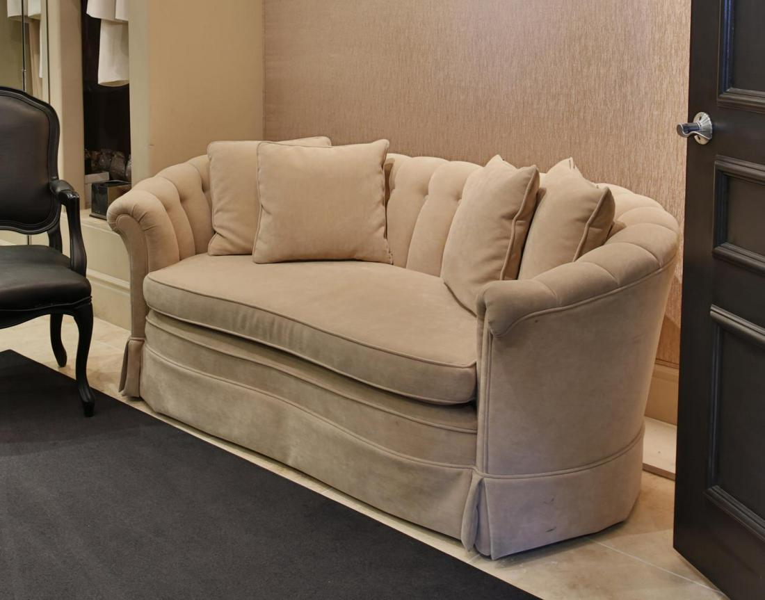 NOLAN MILLER TUFTED SETTEE AND TEAR SHEET: A bone-colored velvet upholstered settee of curved form with button-tufted back, loose seat cushion, and throw pillows. Accompanied by a press clipping of Nolan Miller sitting on the settee. Approxima