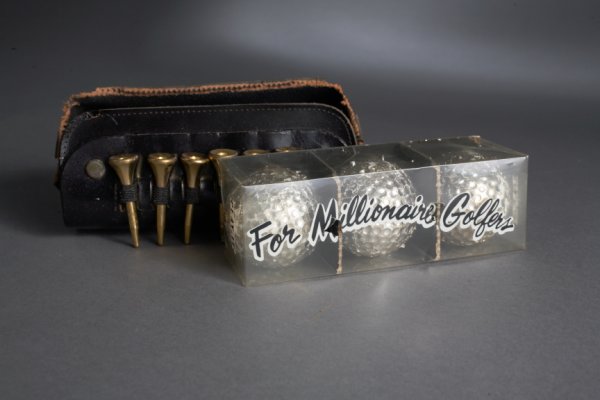 BOB HOPE NOVELTY MILLIONAIRE GOLF BALLS: Three gold tone golf balls in packaged in leather container that read "For Millionaire Golfers" attached to case are six gold painted golf tees. Believed to be a gift from Producer Albert "Cubby" Broc