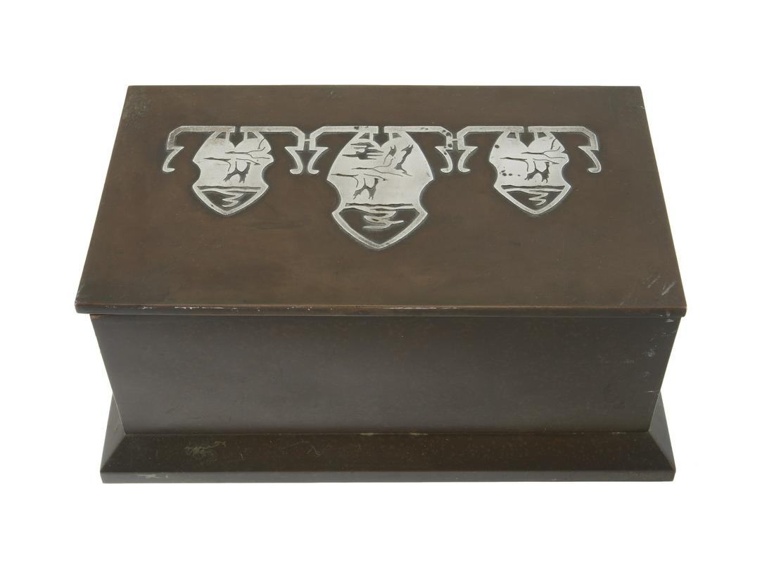 HEINTZ ART METAL SHOP BRONZE CIGAR HUMIDOR: A bronze box decorated with sterling inlaid Native American designs on the lid with a narrow compartment on the inside of the lid, and wood lining the body. Marked "AHMS" on the underside. 3 1/4 by 7 