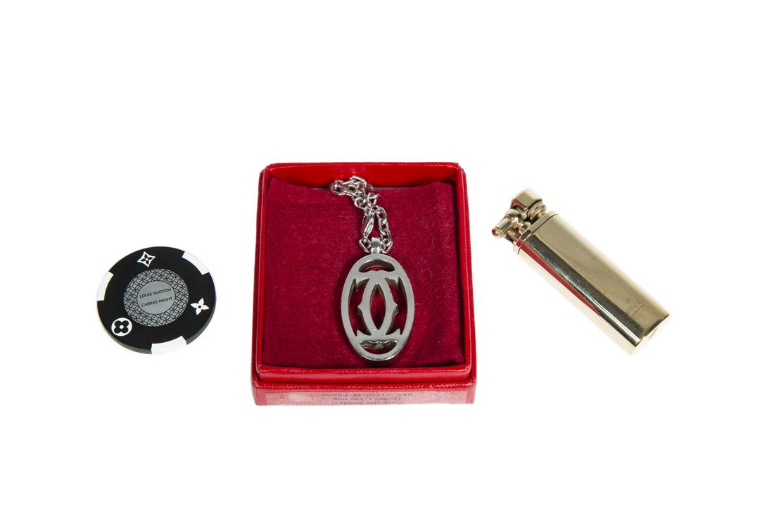 GUCCI GOLD TONE LIGHTER AND OTHER ITEMS: A group of three items: a Gucci gold tone lighter; a Cartier silver tone keychain; and a Louis Vuitton casino night poker chip. Lighter, height, 2 3/4 inches Fine Art