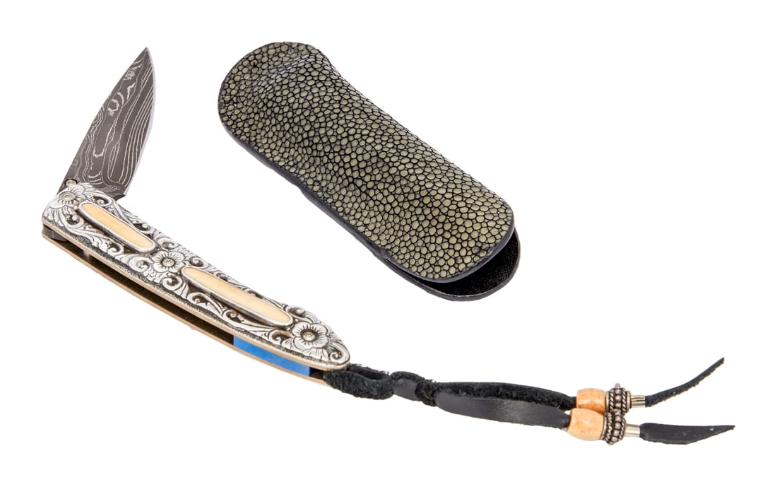 ZZ TOP | DUSTY HILL POCKET KNIFE BY WILLIAM HENRY: A silver floral handle with inset panels of fossilized bone material, leather tassel, spring lock pocket knife with Damascus steel blade marked "WH," with thumb stud. The interior of the kni