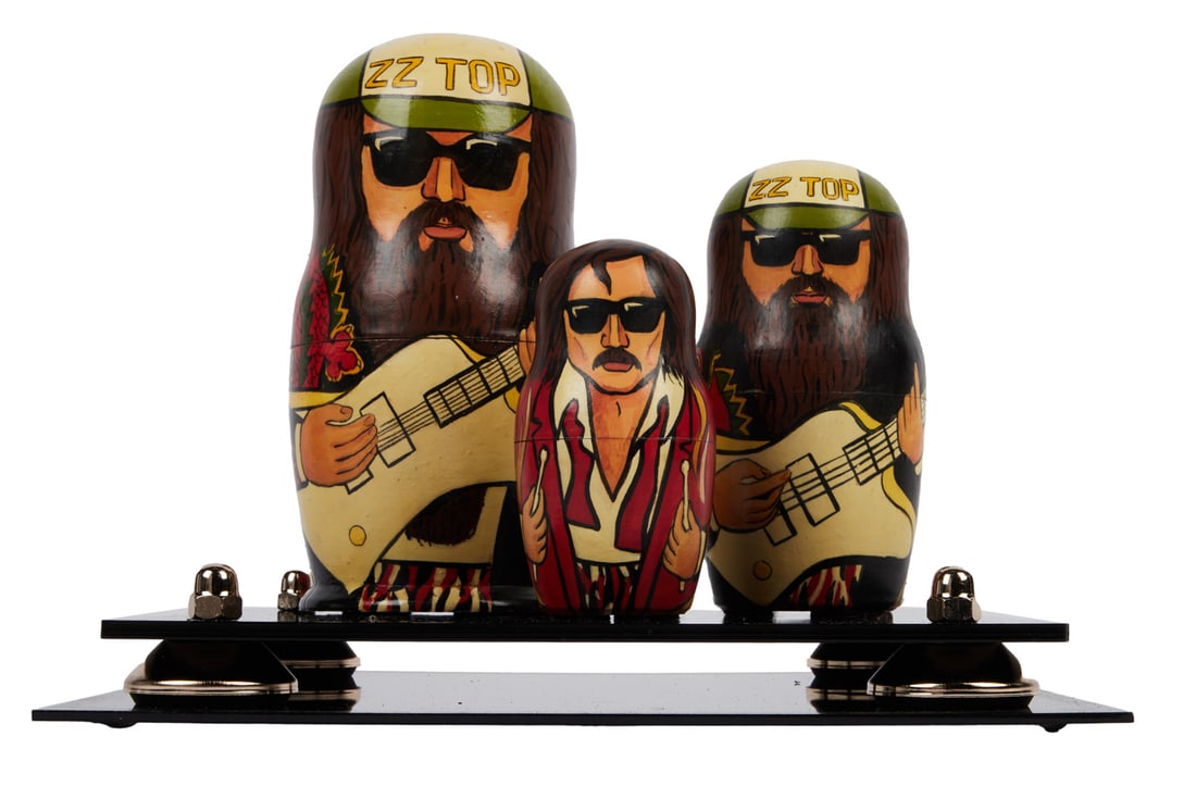 ZZ TOP | DUSTY HILL RUSSIAN NESTING DOLLS: A set of three Russian nesting dolls depicting Dusty Hill, Frank Beard, and Billy Gibbons colorfully painted holding their guitars and drumsticks. Dimensions: Tallest 7 1/2 inches PROVENANCE From The