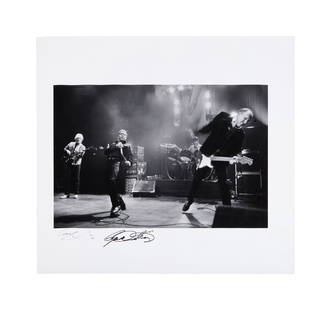 The Who | Limited Edition Mick Hutson Black and White Photograph Signed By Him And Roger Daltrey,: A black and white photograph with a glossy finish depicting Roger Daltrey, Peter Townshend, John Entwistle, and a drummer playing on stage, signed in black felt-tip ink on the left margin by the