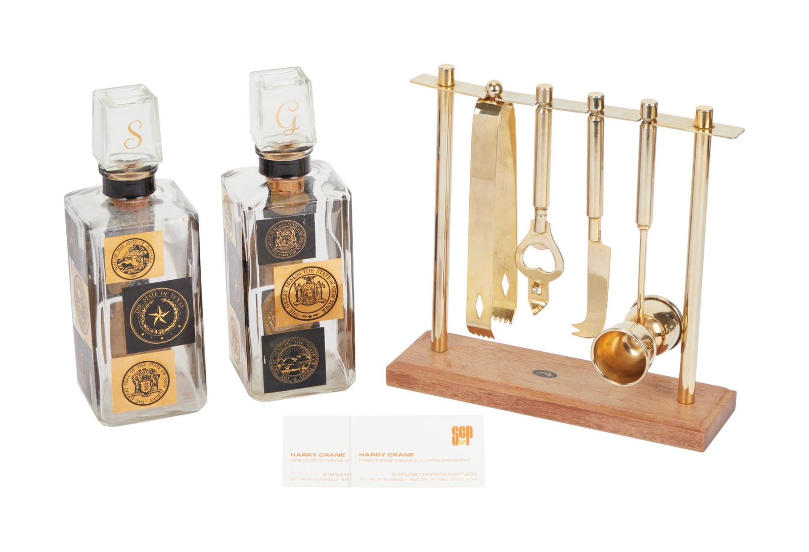 Mad Men | Harry Crane (Rich Sommer) Mid-Century Decanters and Bar Tools: A pair of mid-century glass gin and scotch decanters both with state seal patterns, one stopper is embossed with "G" and the other with "S" and a wood and gold-tone metal boor tool