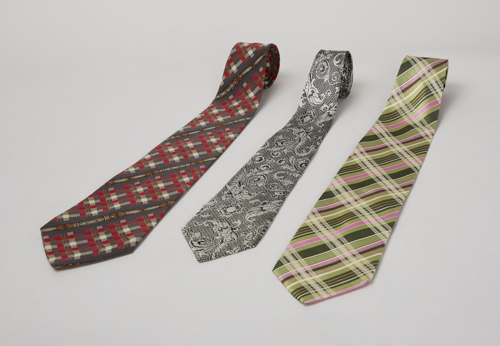 Group of Designer Ties: A lot of three designer neck ties that includes a Brioni 100% silk silver and black paisley, a Gucci red and white plaid on grey silk wool blend and a pink and green plaid silk blend by Kenzo. A tie f