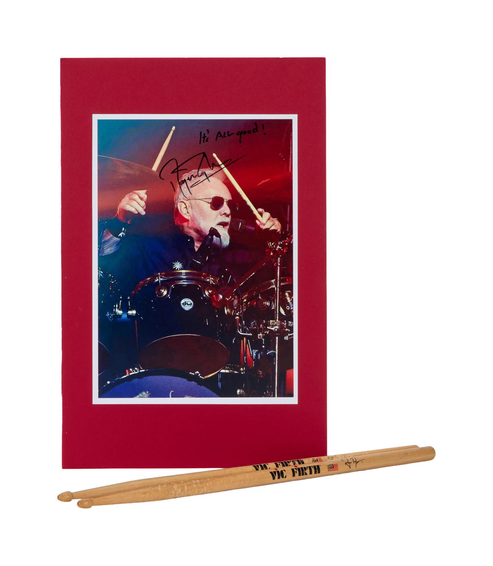Queen | Roger Taylor Signed Photo with Drumsticks: A color photograph of Queen's Roger Taylor playing the drums on stage, signed and inscribed "It's all good!" by him in black marker. Accompanied by a pair of Vic Firth Roger Taylor s