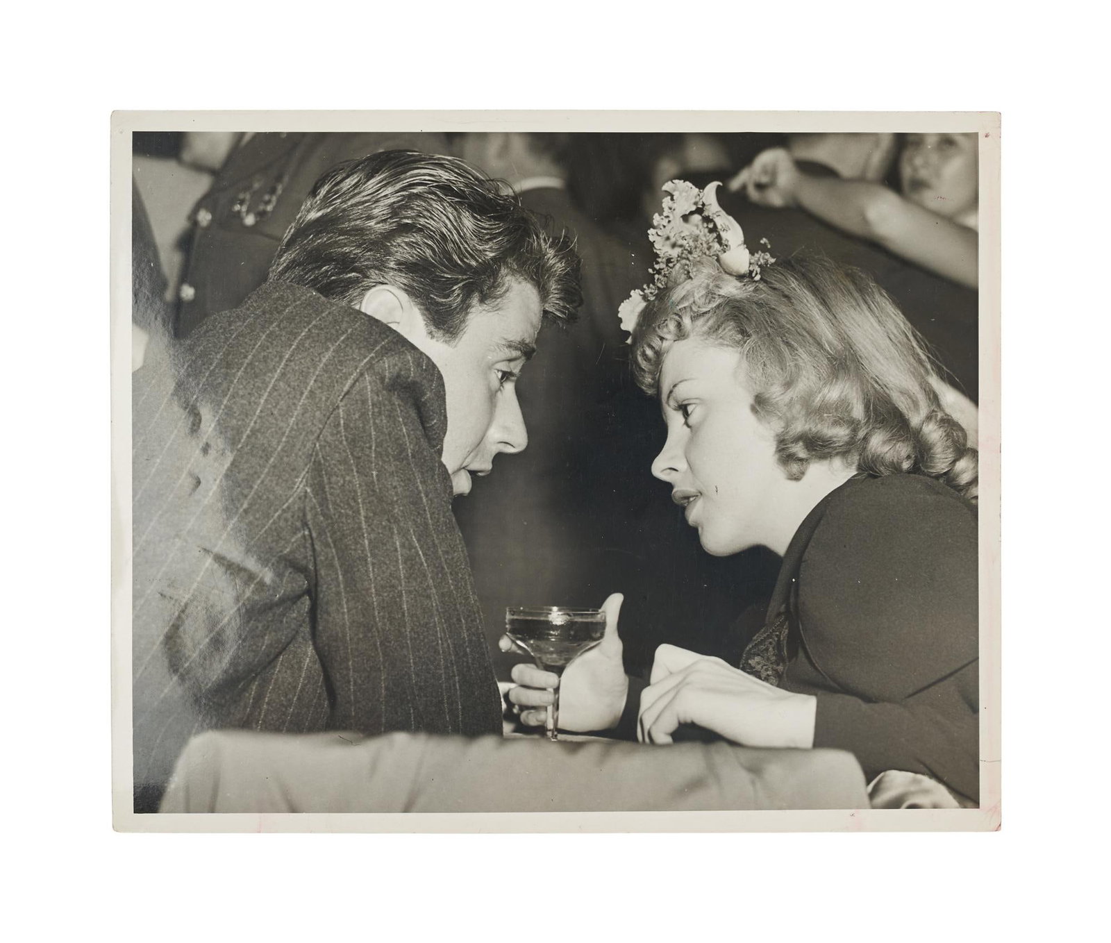 Judy Garland | 1944 Black and White Press Photograph: An original print; glossy finish, weight-and-a-half paper, depicting the 21 year-old star holding a cocktail at Mocambo as she has an intimate conversation with Peter Lawford; verso displays a typed p