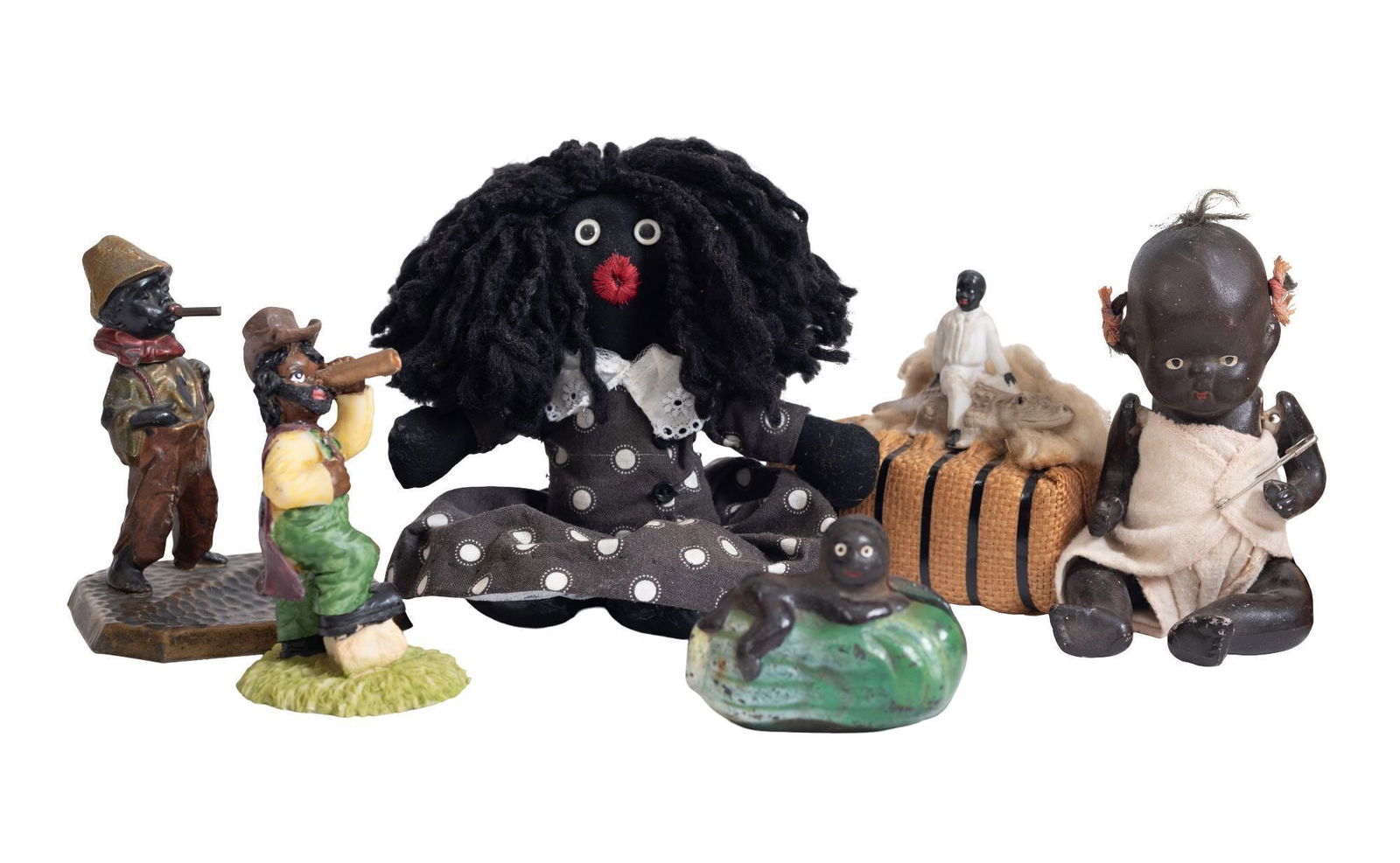 Whoopi Goldberg | Six Assorted Black Americana items: A collection of Black Americana items, including two Golly dolls, a figurine of a boy with a telescope, a cast iron baby on a watermelon penny bank, a plastic baby doll, a fabric Golly doll, a metal s
