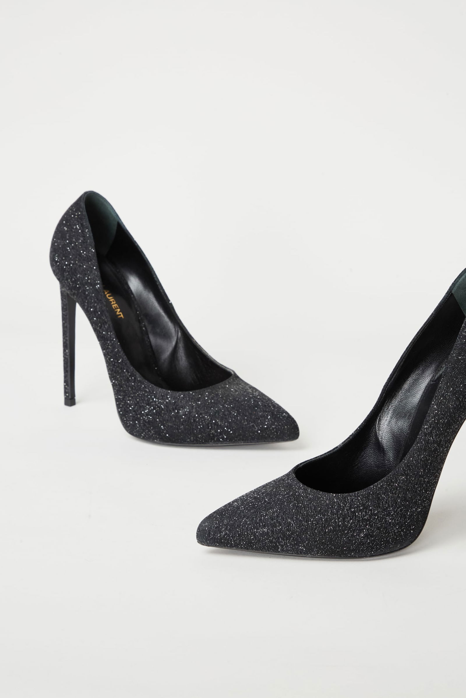 Saint Laurent | Zoe Stiletto Glitter Pumps: A pair of "Zoe" Saint Laurent black glitter pumps with embossed texture. The pumps are 110mm heel-height leather lined with a gilt-gold Saint Laurent stamp. There is wear to the outer soles of the sho