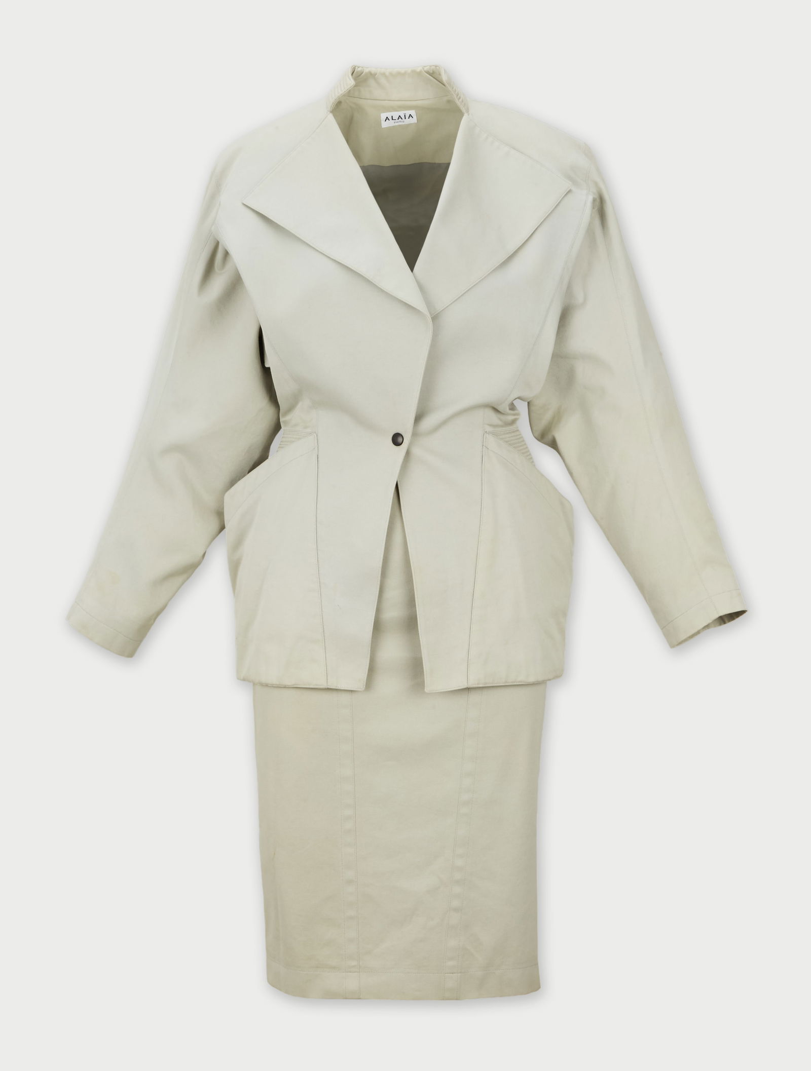 Alaïa Paris | 1982 sand-tone Jacket and Skirt ensemble: Alaïa Paris sand-tone cotton twill jacket and skirt ensemble circa 1982.The jacket has sharp notched lapel and an open front secured by one snap closure. The jacket has ribbed panel detailing at