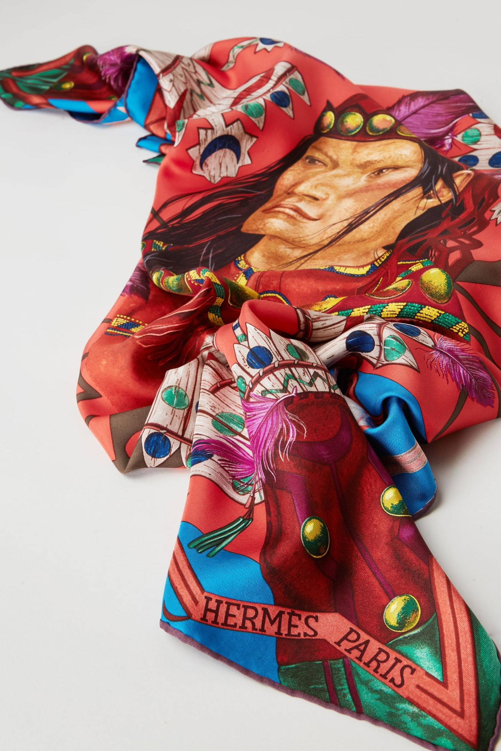 Hermès | Pani La Shar Pawnee Silk Scarf: Hermès silk twill scarf titled "Pani La Shar Pawnee" and designed by artist Kermit Oliver.The scarf features a central portrait of a Pawnee chief on a vibrant vermilion red ground. The figure is