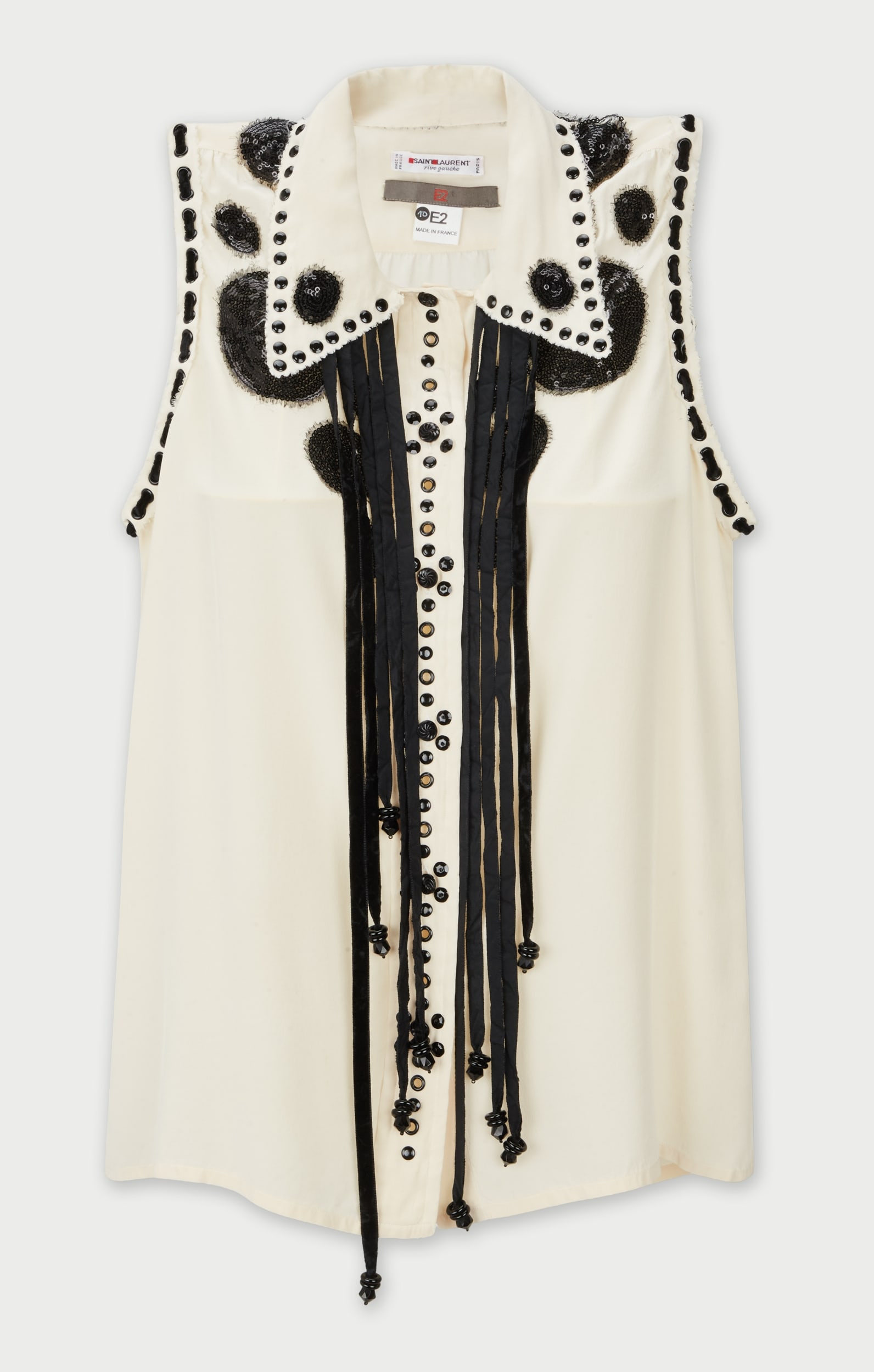 Saint Laurent | Vintage Embellished Blouse: A vintage Saint Laurent sleeveless blouse upcyled by E2 composed in ivory silk with striking black contrast details.Designed with a pointed collar and button-front closure the blouse is accented by st