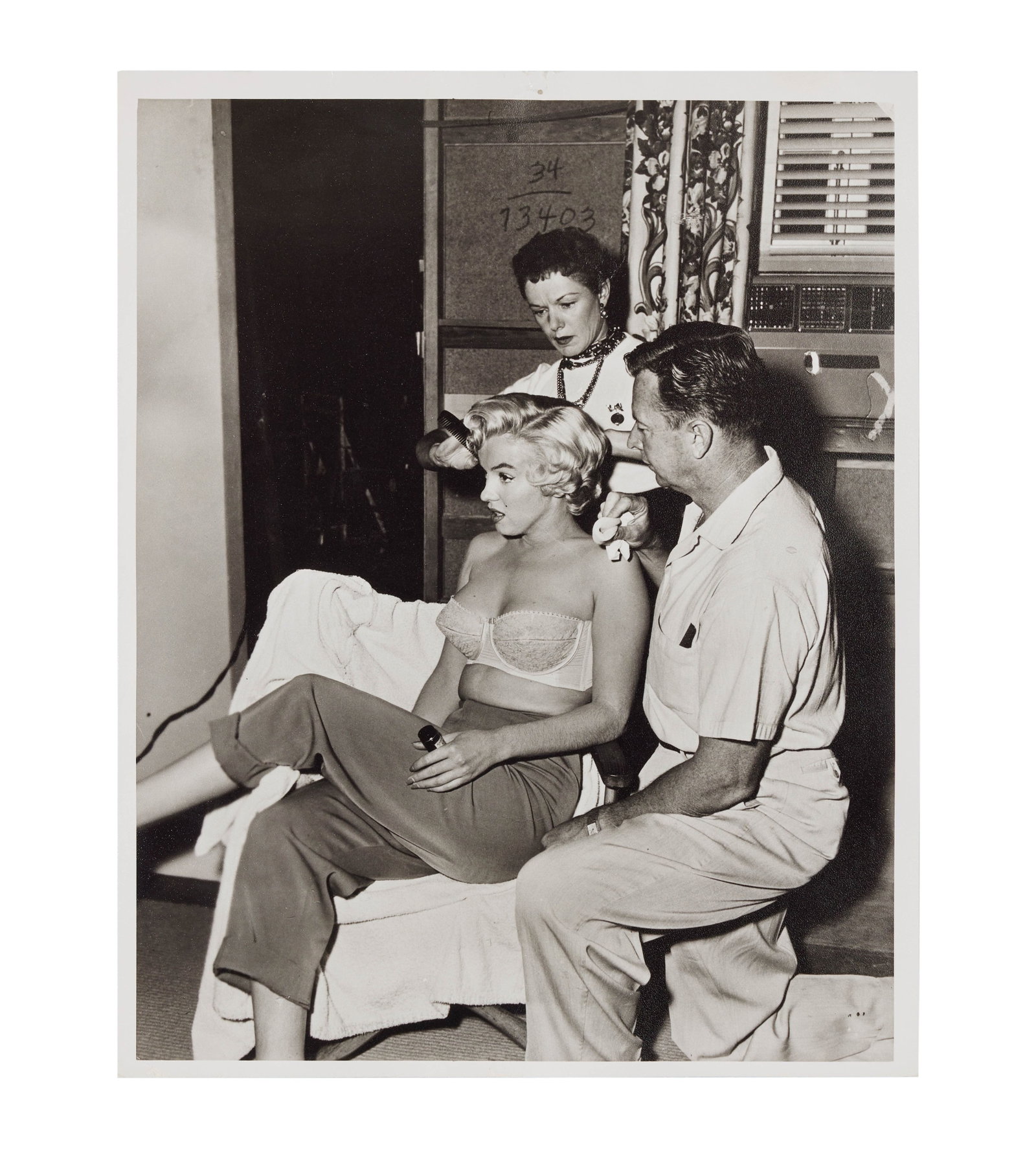 Marilyn Monroe | 1954 Rare Black and White Photograph with Her Make-Up Team: An original print; matte finish, double-weight paper, depicting the star on the set of her 1955 20th Century Fox comedy "The Seven Year Itch" as her make-up man, Allan "Whitey" Snyder, and her hairdre