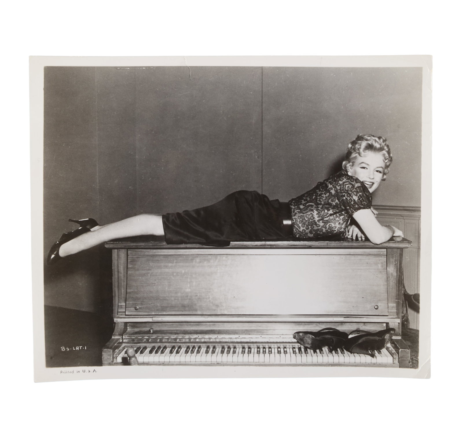 Marilyn Monroe | 1956 Black and White Photograph by Cecil Smith Related to "Bus Stop": An original print; glossy finish, depicting the star posing atop a piano wearing a costume from her 1956 20th Century Fox drama, verso with a typed press snipe reading in part "The ?New' Marilyn Monro