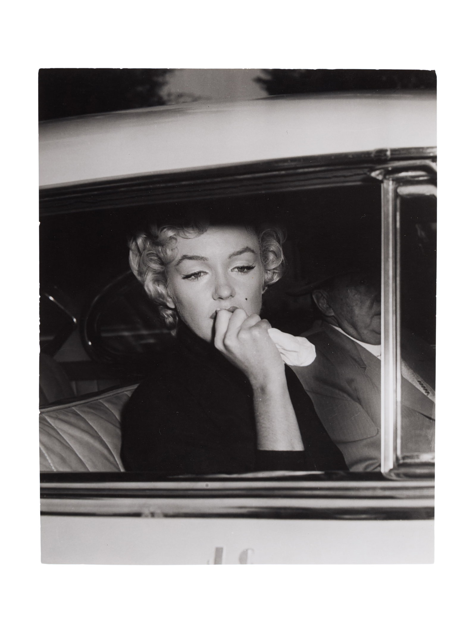 Marilyn Monroe | 1954/1970s Black and White Photograph: A circa 1970s later print; semi-gloss finish, double-weight paper, depicting the star sitting inside a car next to attorney Jerry Giesler on October 6, 1954, just after she publicly announced she was 