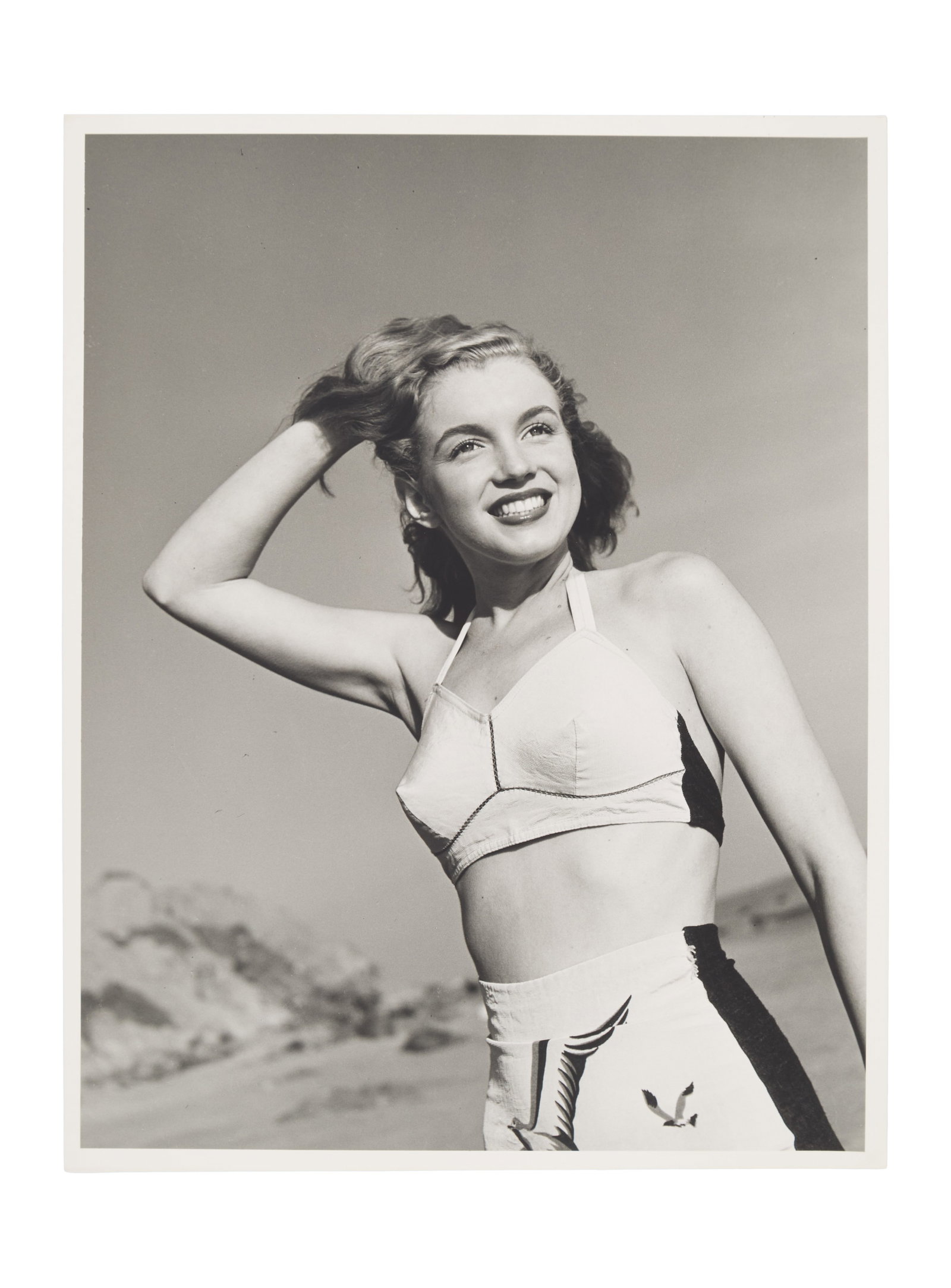 Marilyn Monroe | 1946/1990s Black and White Photograph by Joseph Jasgur: A circa 1990s later print; matte finish, double-weight paper, depicting the 19 year-old model wearing her well-known "seagull" bathing suit as she poses on Zuma Beach in Malibu; originally from the pe