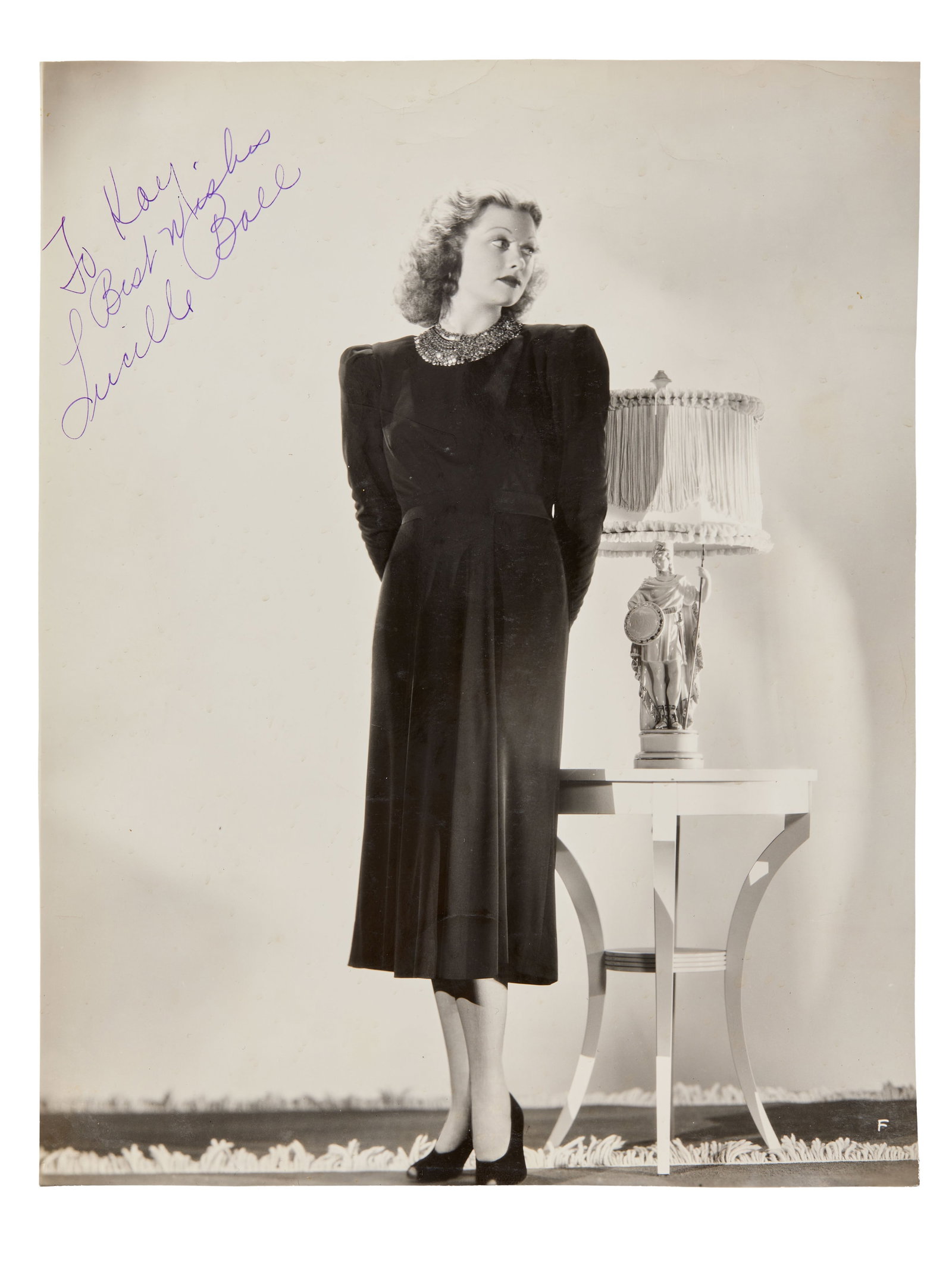 Lucille Ball | Signed 1938 Photograph: 1938, original print; glossy finish. A studio photograph of the great comedienne Lucille Ball, standing and looking to the side in a dark dress and heels with a tiered necklace. Ball signed the photo