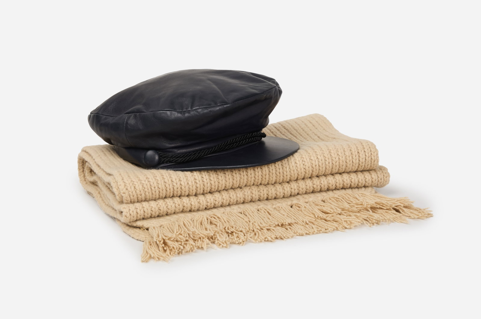 Hermès | Cashmere Scarf and Unlabeled Leather Hat: A Hermès cashmere scarf and an unlabeled leather military hat from the collection of Cameron Silver. The knit tan scarf is composed of 100% cashmere, and it has fringe ends. The back of the