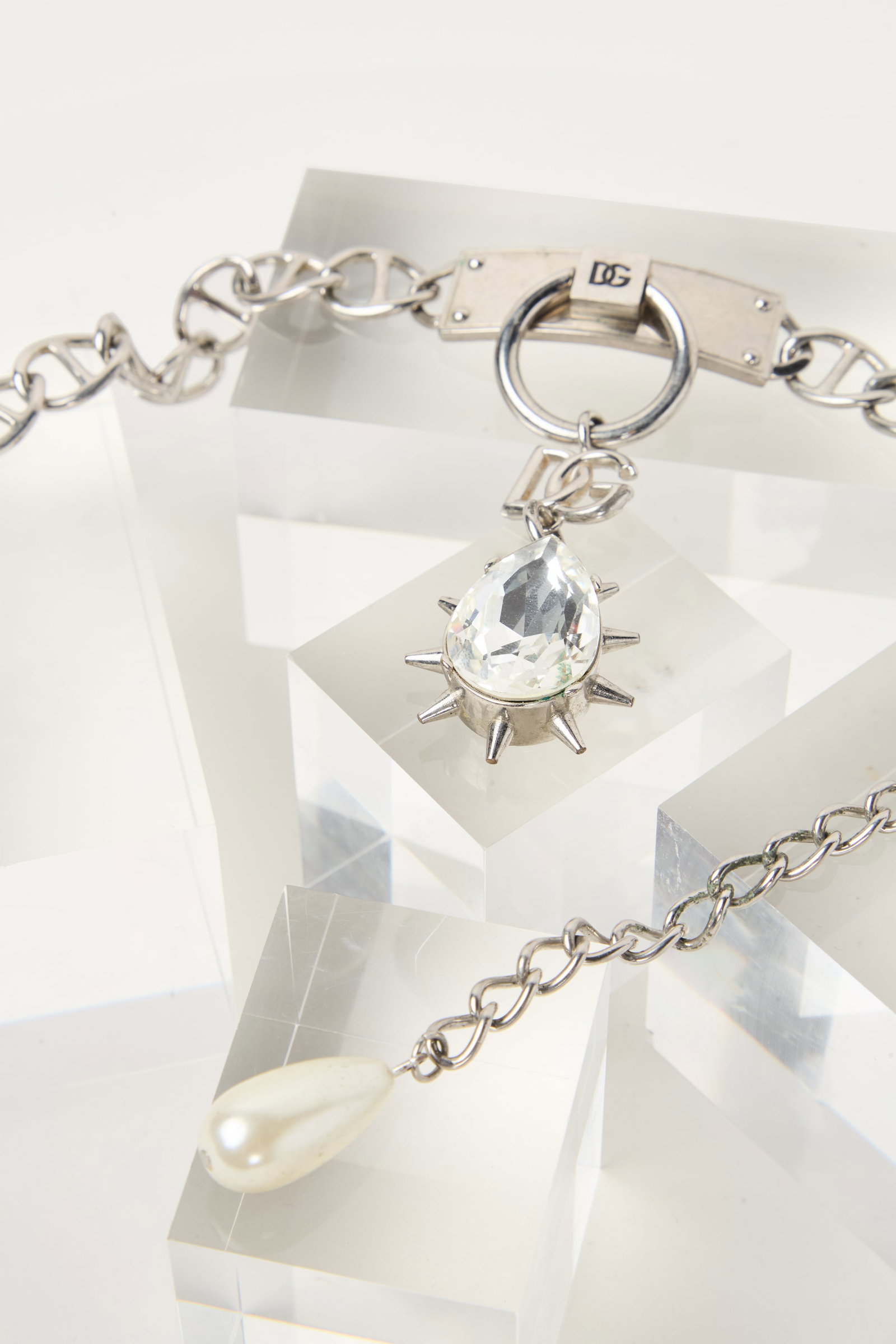 Dolce & Gabbana | Silver DG Pendent Chocker: A Dolce & Gabbana silver tone chain link chocker with DG monogram at the front with a pear shape spiked faux diamond. The necklace has a chain link extender with a faux-pearl drop. From the