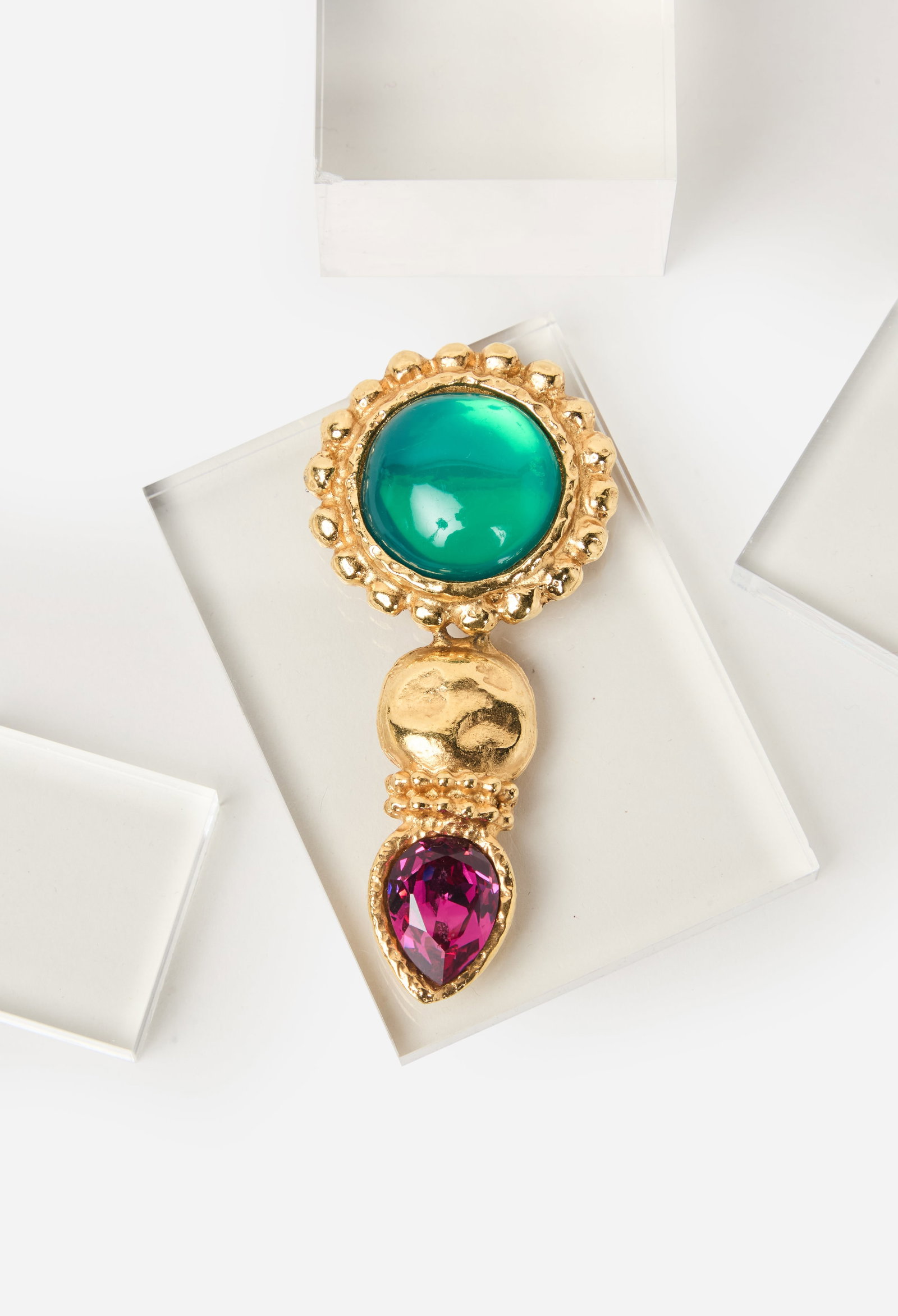 Ungaro | Jeweled Brooch: Ungaro Costume Brooch featuring a large simulated green cabochon set within a textured gold-tone surround, suspending a pear-shaped purple rhinestone pendant. 3 3/4 x 1 3/4 inches. Marked "EU Paris