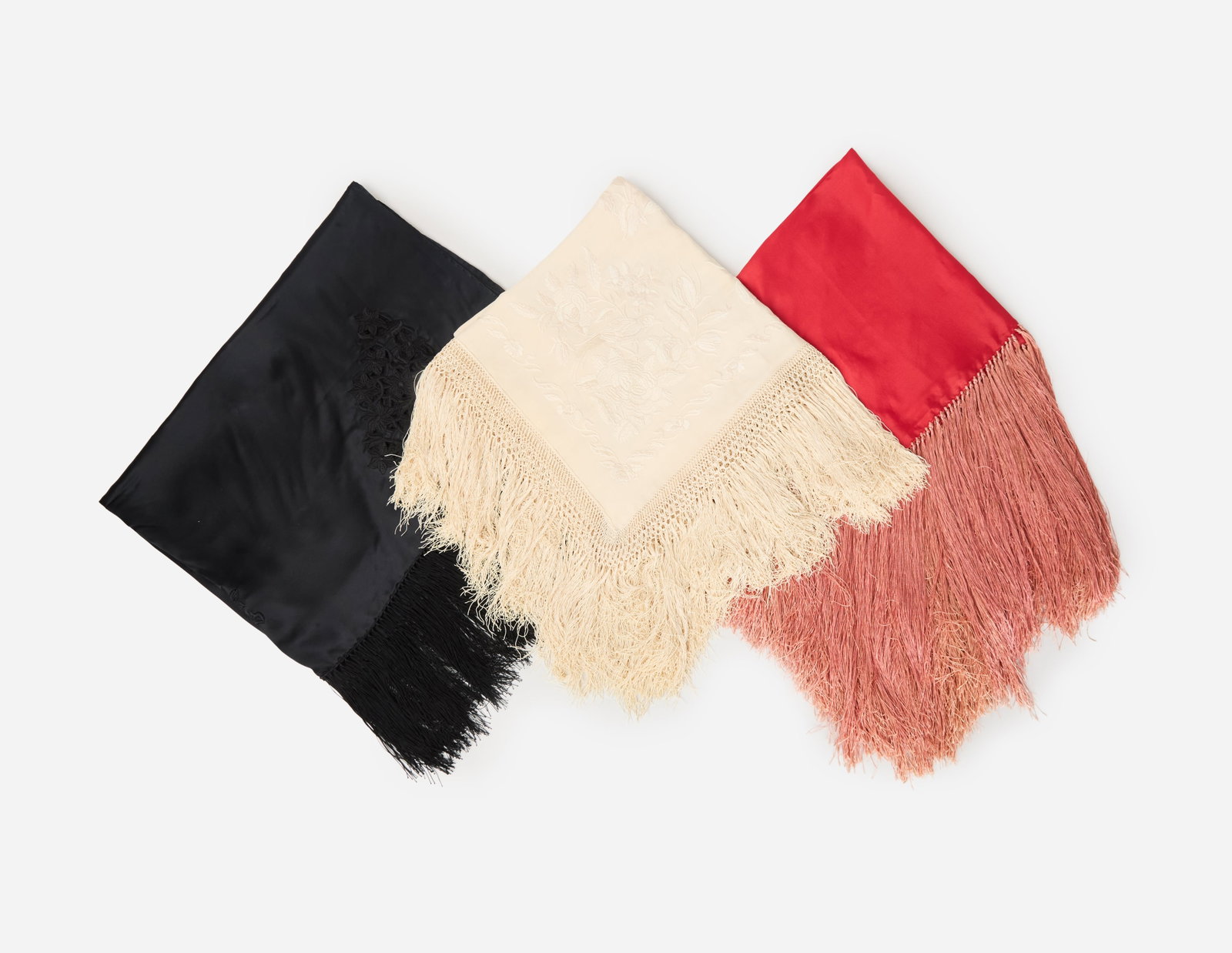 Vintage | Three Silk Fringe Shawls: A group of three vintage silk fringe shawls. The first shawl is red with pink fringe along each end. The second shawl is white with floral embroidery and matching fringe. The final shawl is black