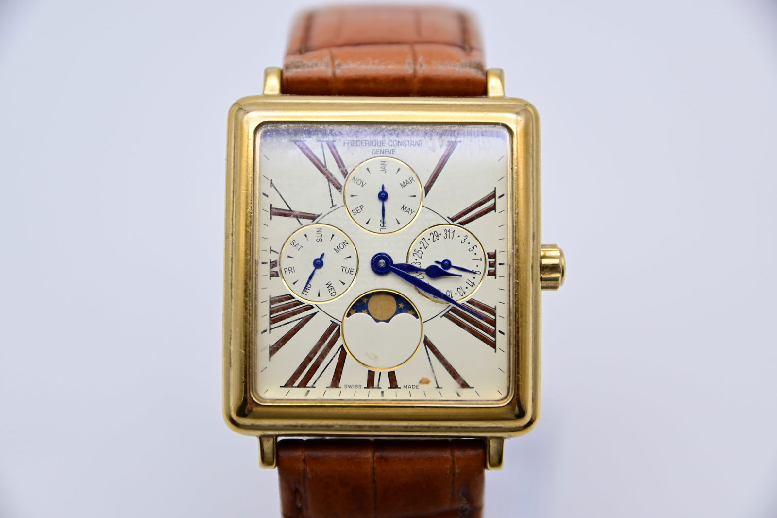 Frederique Constant Persuasion Mondphasen-Quarzuhr mit weißern Zifferblatt FC-265X3C24/6: Gelbvergoldetes Edelstahlgehäuse mit braunem Lederarmband. Feste gelbvergoldete Lünette. Silbernes Zifferblatt mit schwarzen Zeigern und römischen Stundenmarkierungen.