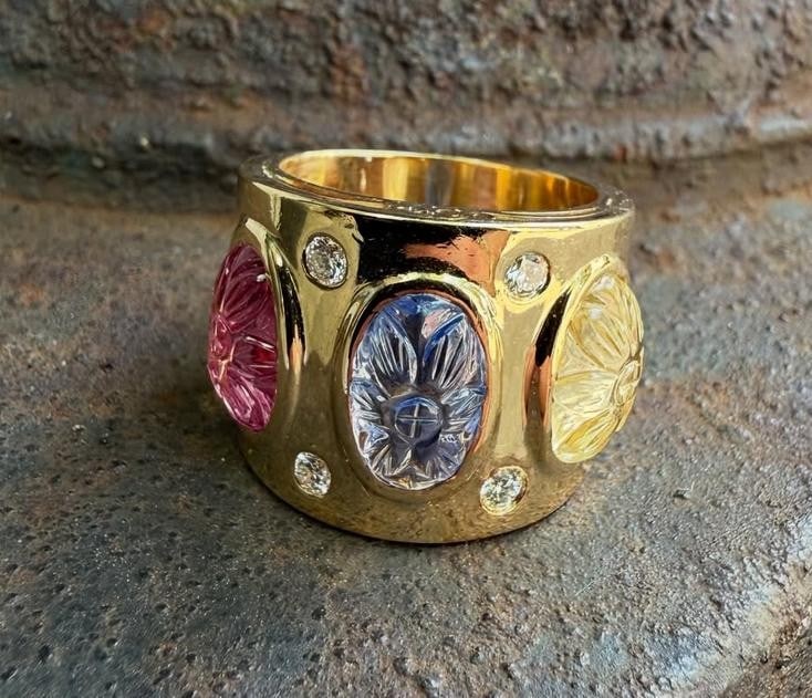 18k Gold GIA Carved Pink Spinel Yellow Blue Sapphire Cigar Band: 18k Gold GIA Carved Pink Spinel Yellow Blue Sapphire Cigar Band This exquisite 18k Gold Cigar Band Ring showcases a stunning collection of gemstones, including a rare GIA-certified 8.36ctw Carved Pink