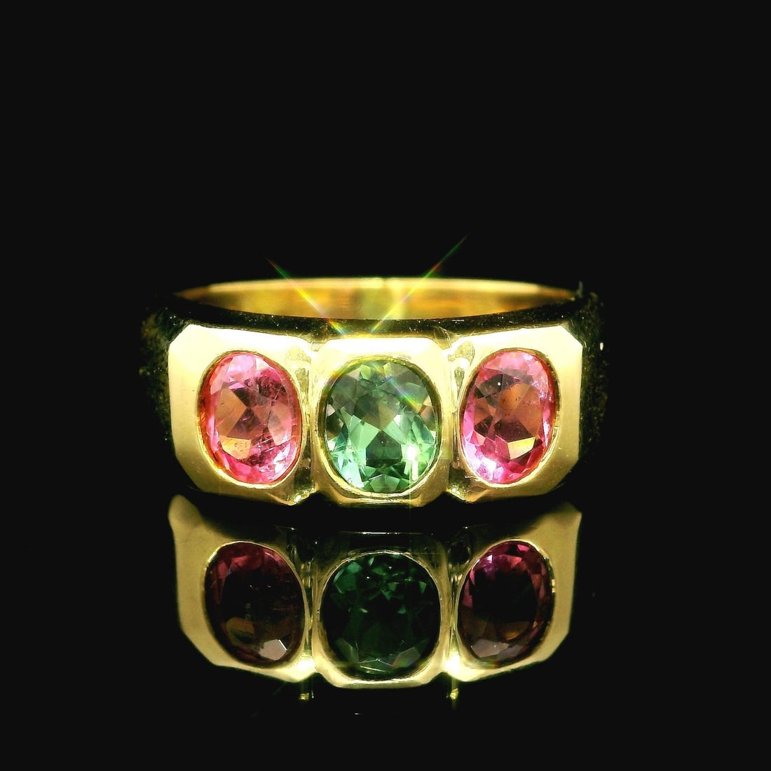 18k Yellow Gold Three Stone Tourmaline Band Ring: 18k Yellow Gold Three Stone Tourmaline Band Ring This stunning 18k yellow gold cocktail ring features a unique three-stone design with vibrant natural tourmalines. The ring showcases two oval-cut pink