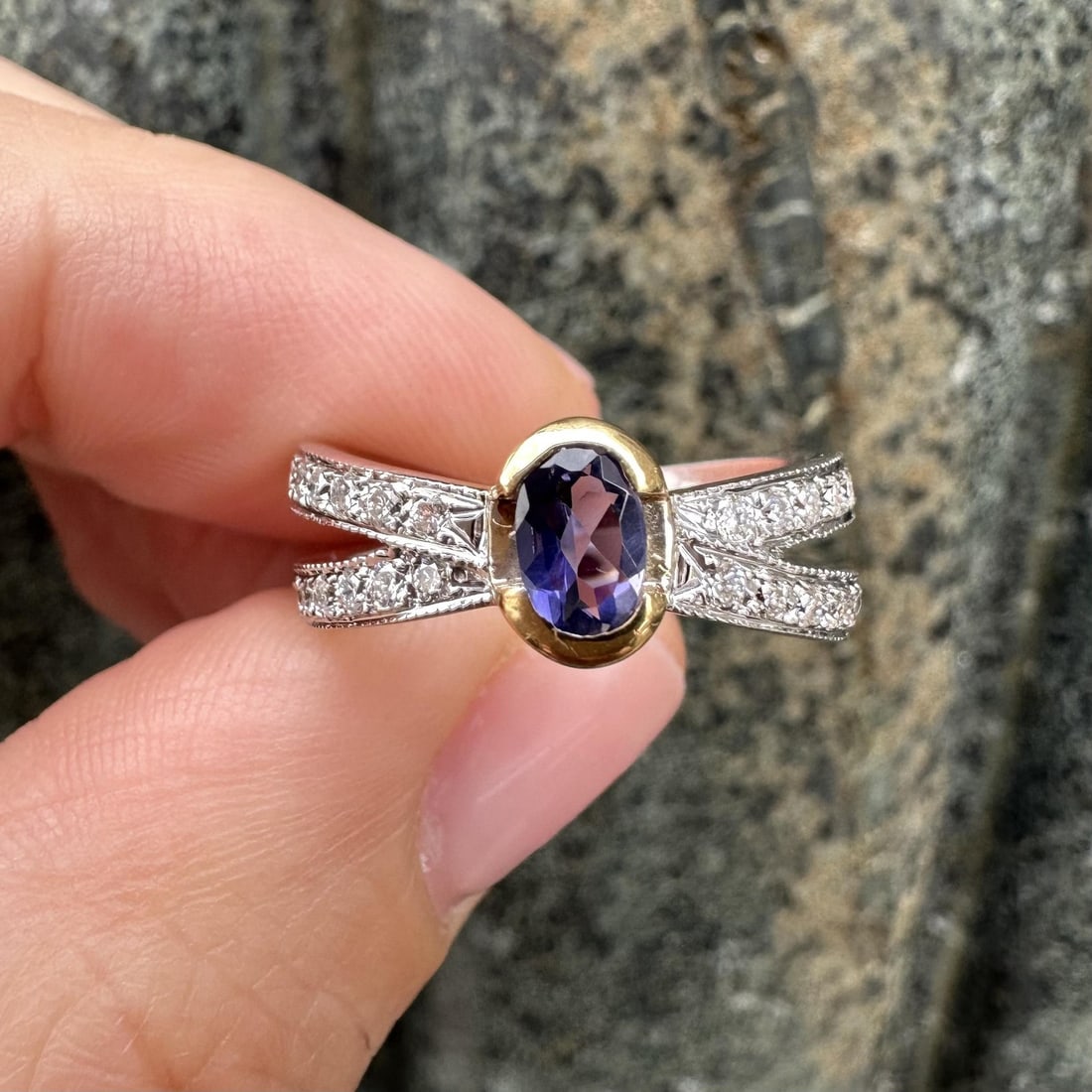 18k Yellow and White Gold Ring with Bluish Violet Gem and Diamond Accents: 18k Yellow and White Gold Ring with Bluish Violet Gem and Diamond Accents This elegant cocktail ring features a natural oval-cut bluish violet stone set in a half bezel, accented with 24 round brillia