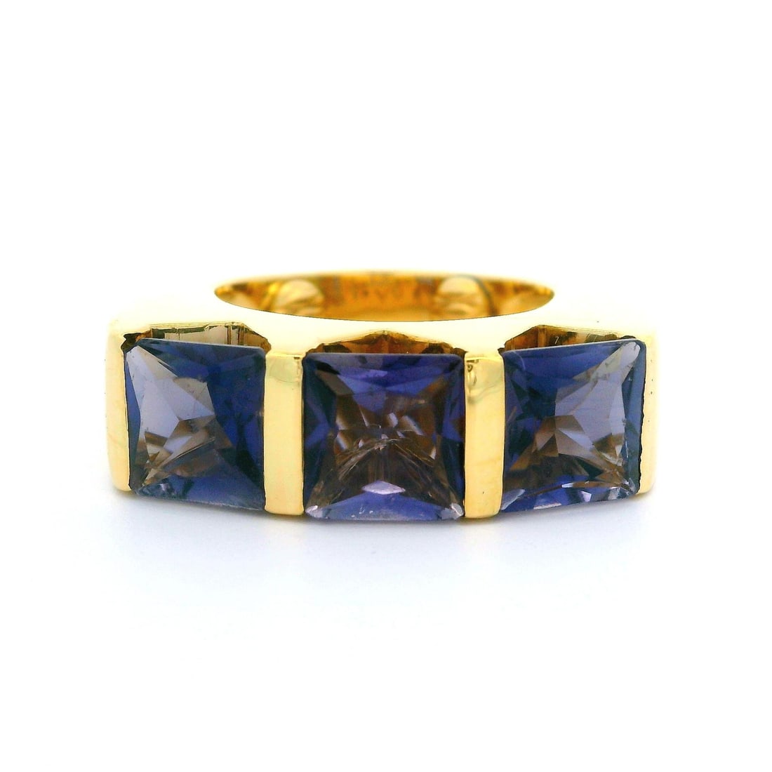 18k Yellow Gold Channel Set Iolite Band Ring with 3 Square Cut Stones: 18k Yellow Gold Channel Set Iolite Band Ring with 3 Square Cut Stones This striking band ring features a substantial design crafted from solid 18k yellow gold. It showcases three natural, genuine ioli