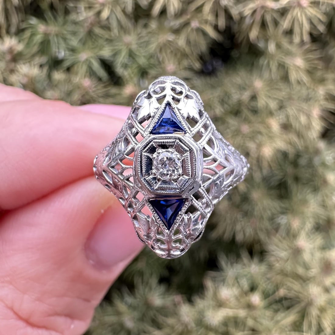 18k White Gold Art Deco Filigree Ring with Diamond and Sapphire Accents: 18k White Gold Art Deco Filigree Ring with Diamond and Sapphire Accents This Art Deco dinner ring features a detailed filigree design meticulously hand engraved in solid 18k white gold. The centerpiec