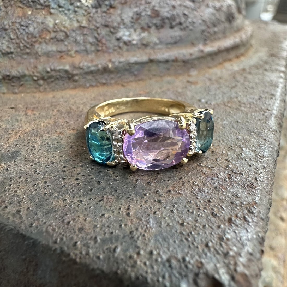 Three Stone 14k Yellow Gold Ring with Amethyst Blue Topaz and Diamonds: Three Stone 14k Yellow Gold Ring with Amethyst Blue Topaz and Diamonds This elegant cocktail ring features a natural oval-cut amethyst as the centerpiece, accented by two natural London blue topaz sto