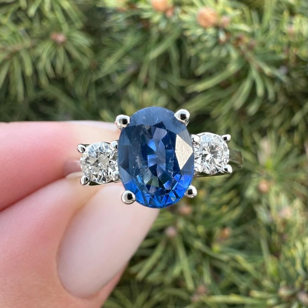 Oval Blue Sapphire and Diamond Three Stone Ring in 14k White Gold: Oval Blue Sapphire and Diamond Three Stone Ring in 14k White Gold This elegant cocktail ring features a natural oval-cut blue sapphire as the centerpiece, accented by two round brilliant-cut natural d