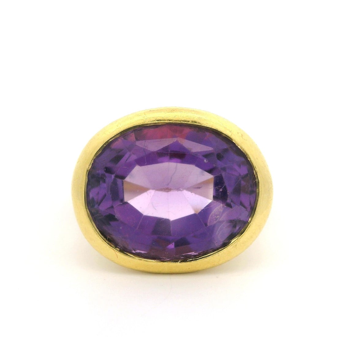 18K Yellow Gold 7.5ct Oval Amethyst Solitaire Ring Textured Finish: 18K Yellow Gold 7.5ct Oval Amethyst Solitaire Ring Textured Finish This exquisite 18k Yellow Gold ring features a stunning 7.5ct oval cut amethyst, elegantly bezel set to showcase its rich purple colo