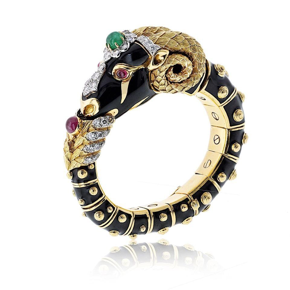 Vintage Ram Motif Bangle in 18K Gold with Emeralds and Diamonds by David Webb: Vintage Ram Motif Bangle in 18K Gold with Emeralds and Diamonds by David Webb This vintage bangle bracelet by David Webb features the brand's iconic ram motif, expertly crafted in 18K yellow gold. The