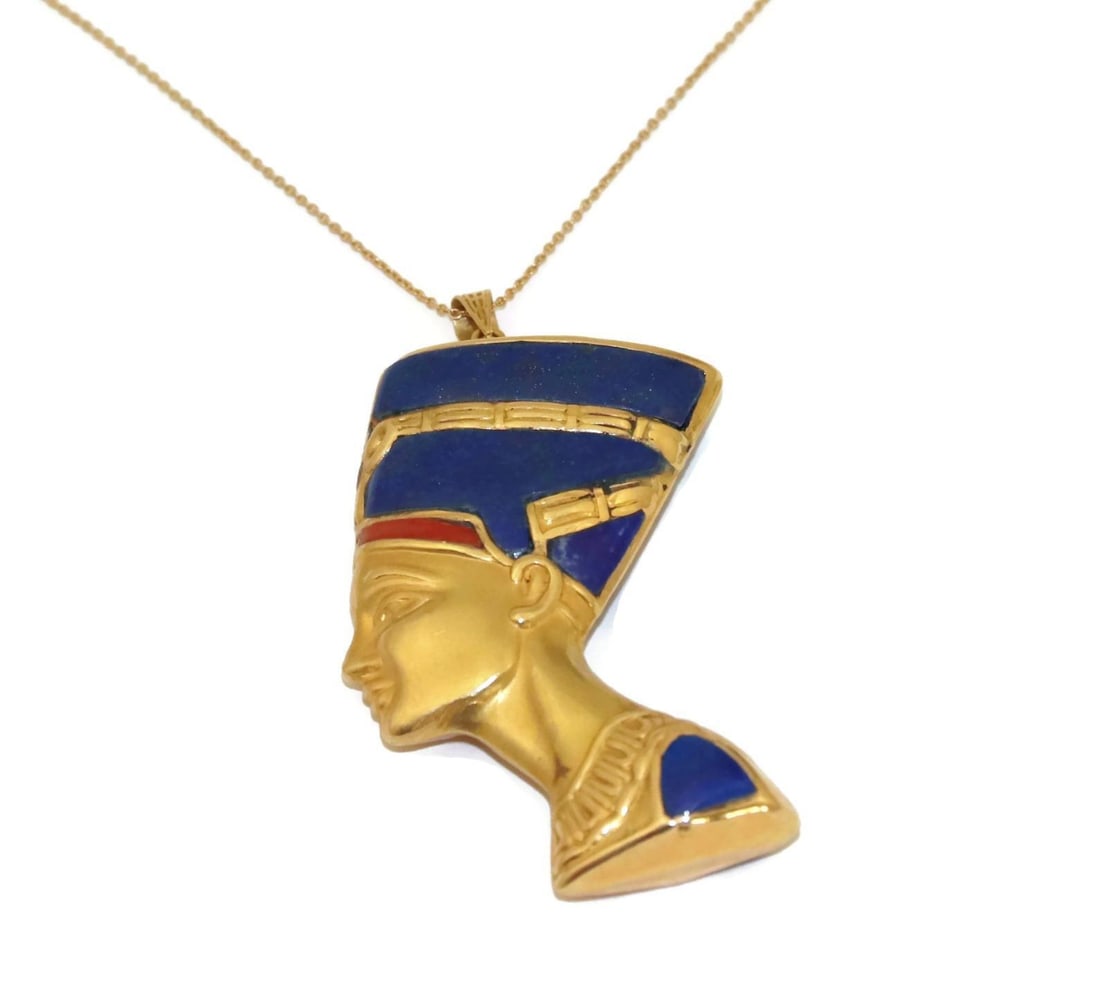 Nefertiti 18k Gold Lapis Coral Pendant Necklace: Nefertiti 18k Gold Lapis Coral Pendant Necklace This remarkable pendant necklace features a detailed sculpted depiction of the renowned Egyptian queen Nefertiti. Crafted from 18k yellow gold with a sm