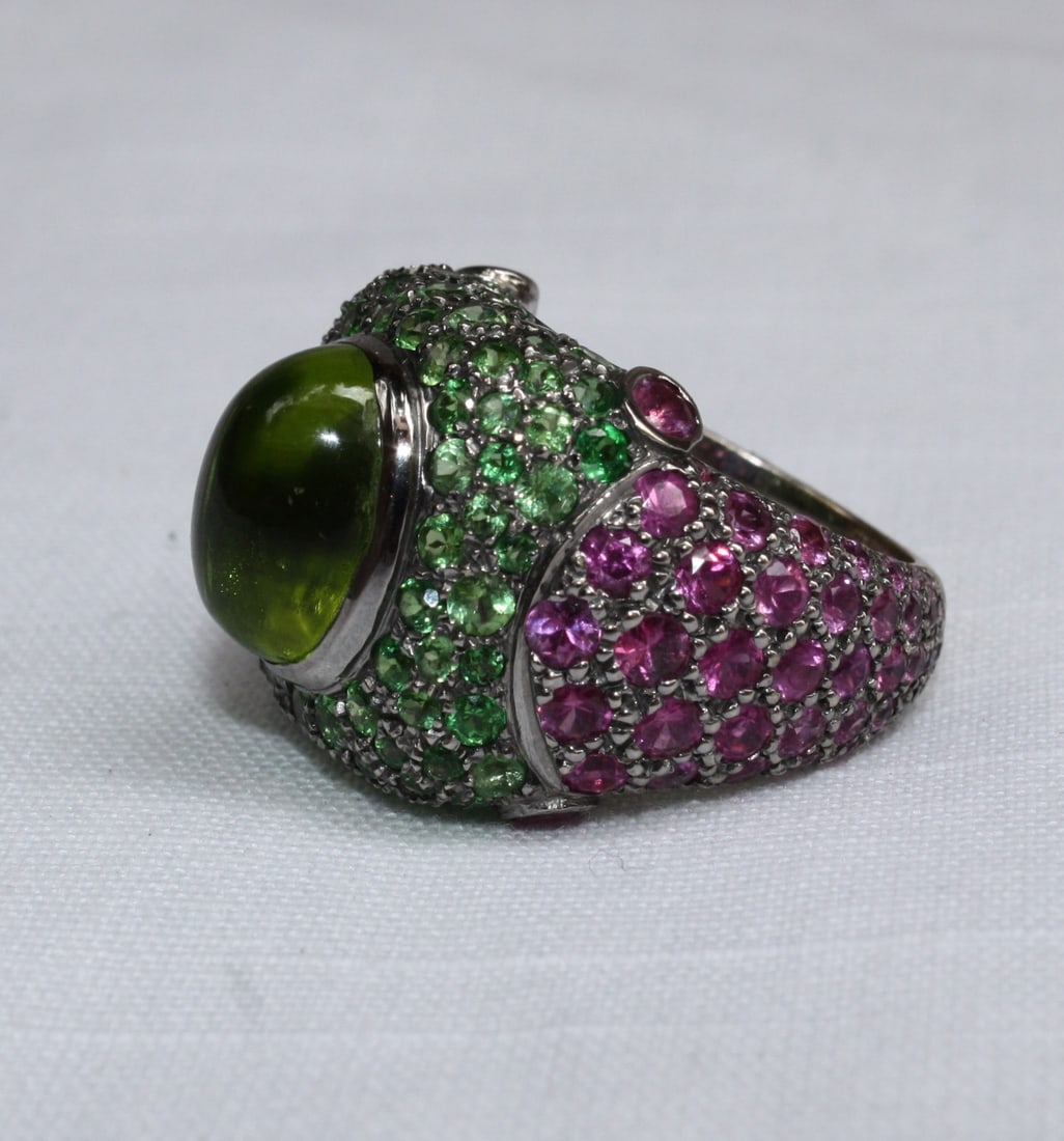 French 18K White Gold Ring with Peridot Garnet Pink Sapphire: French 18K White Gold Ring with Peridot Garnet Pink Sapphire This exquisite French ring features a stunning combination of gemstones set in 18K white gold. At its center is an oval-shaped Peridot cabo