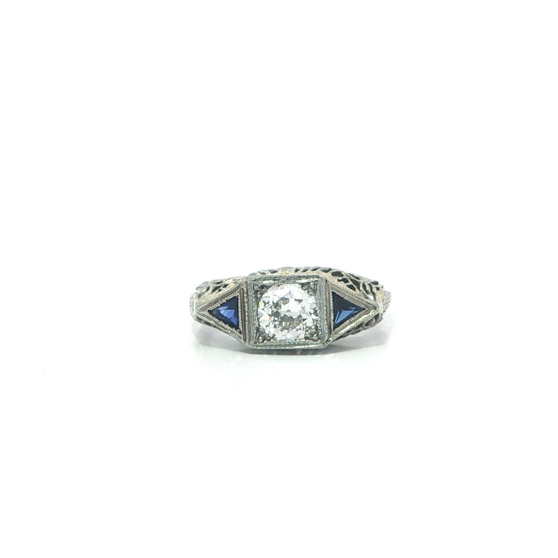 Art Deco Filigree Ring in 18k White Gold with Diamond and Trillion Blue Sapphires: Art Deco Filigree Ring in 18k White Gold with Diamond and Trillion Blue Sapphires This antique Art Deco ring features a 0.41 carat natural old European cut diamond set in solid 18k white gold. The cen