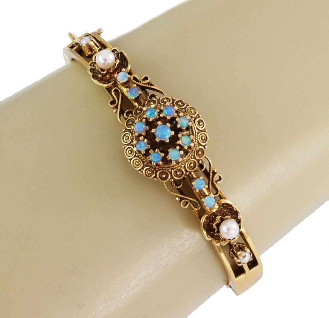 Vintage 14k Yellow Gold Hinged Bangle with Opals and Seed Pearls: Vintage 14k Yellow Gold Hinged Bangle with Opals and Seed Pearls This vintage estate bangle bracelet is crafted in solid 14k yellow gold and features cabochon opals accented with seed pearls. It has a
